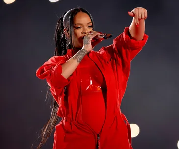 Rihanna performs at the halftime show in a bold red outfit and ponytail, with dramatic stage lighting.