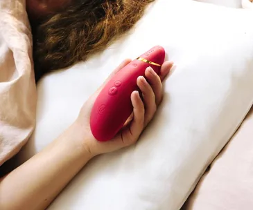 A person holding a red handheld massager with buttons, lying on a pillow.