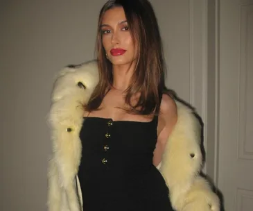 Young woman in a black dress and fur stole, posing indoors with a confident expression.