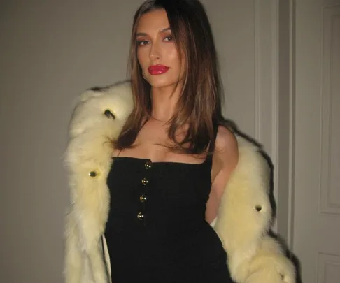 Young woman in a black dress and fur stole, posing indoors with a confident expression.