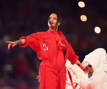 Rihanna performs at the Super Bowl in a red jumpsuit, surrounded by dancers in white outfits.