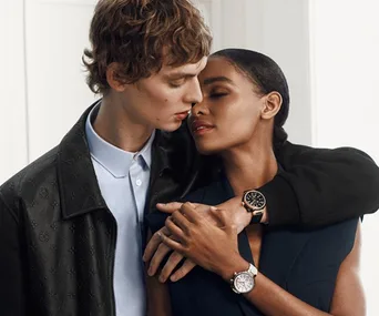 A couple embraces closely, both wearing elegant Louis Vuitton watches, highlighting romance and style.