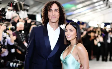 A couple poses on a red carpet event, surrounded by photographers and bright lights.