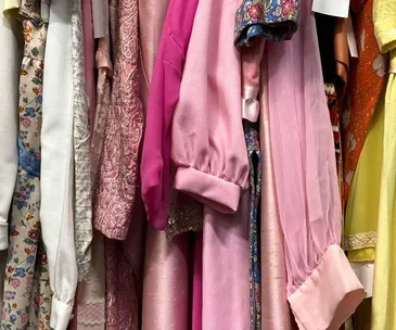 A rack of vintage clothing in various shades of pink, including floral patterns and lace details, hanging closely together.