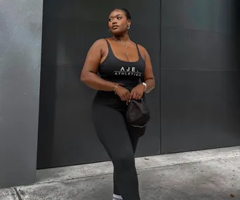 Woman in black Aje Athletica activewear poses confidently against a dark wall.