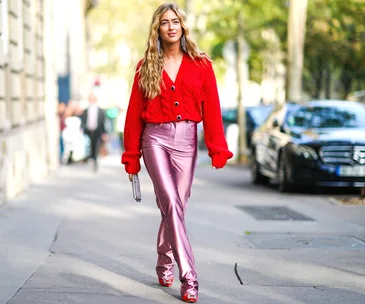 Woman in red sweater and pink metallic pants walking on a city street.