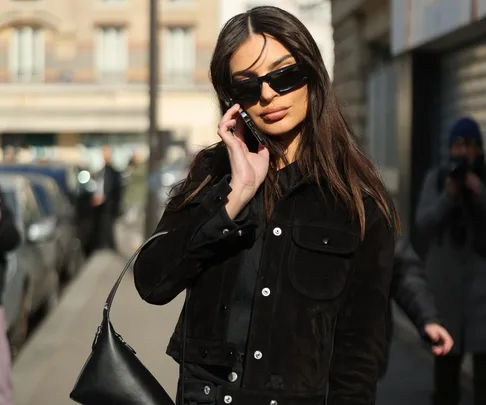 Woman in black jacket and sunglasses on phone at Paris Fashion Week street style.