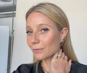 Blonde woman with light makeup and earrings, looking into the camera with a soft smile.