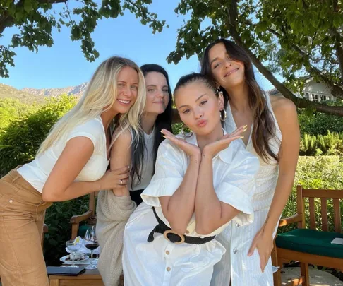 Four women posing together outdoors under a tree, smiling at the camera.