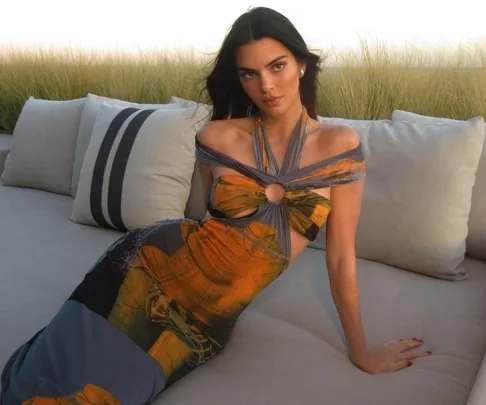A woman in a colorful gown sitting on a couch outdoors, with tall grasses in the background.
