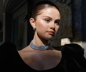 Woman in a black dress and elegant necklace, posed elegantly with natural lighting highlighting her features.