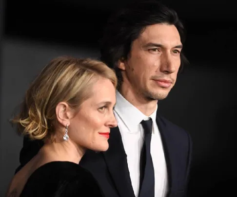 A couple posing elegantly at an event, one wearing a dark suit and the other a black dress with diamond earrings.