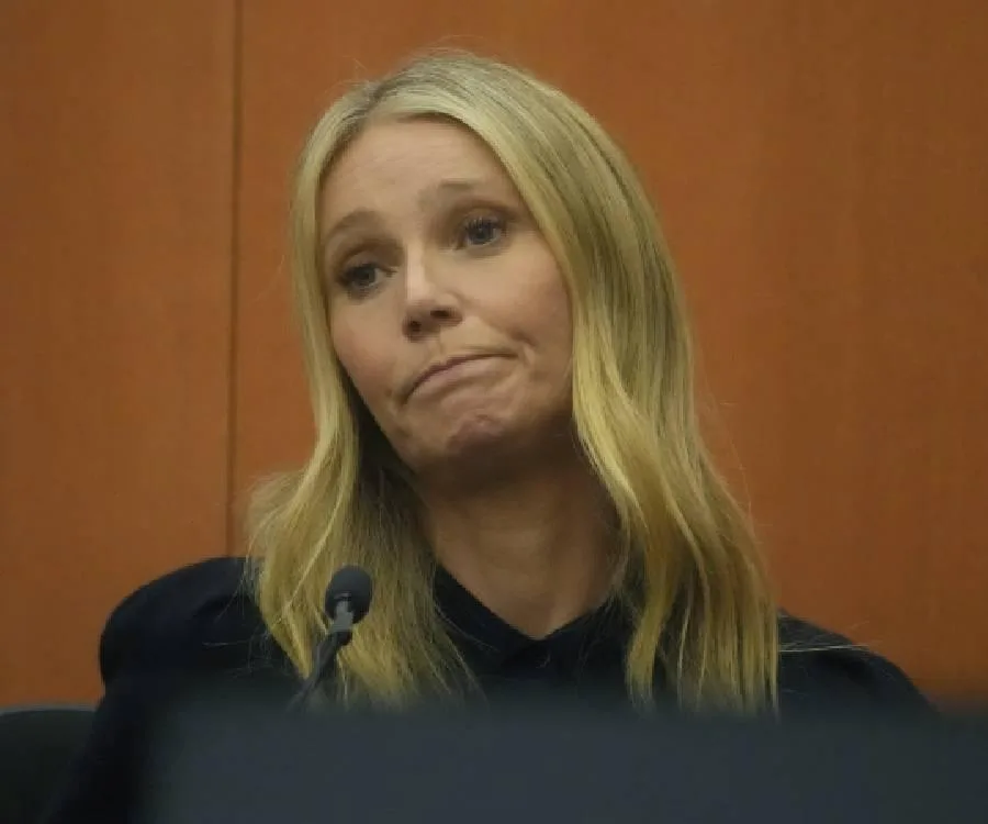 Person with long blonde hair at a microphone in court, looking contemplative.