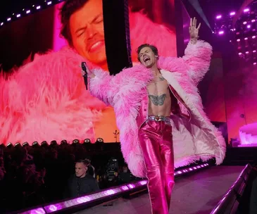 Harry Styles performs energetically on stage in a pink outfit during Love On Tour, Australia, with large screen backdrop.