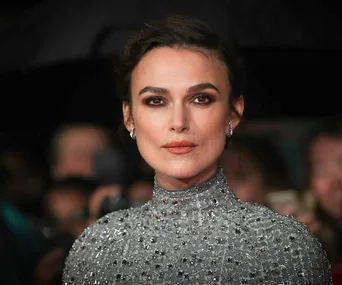 Actress in a sequined dress poses at an event, with a focused expression, surrounded by a crowd.