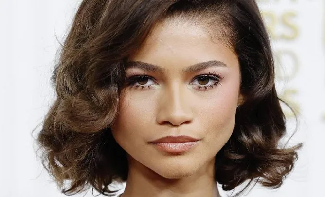 Zendaya with wavy hair, looking directly at the camera at a red carpet event.