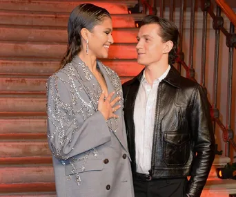 A couple on a staircase; the woman wears a jeweled blazer, the man wears a leather jacket.