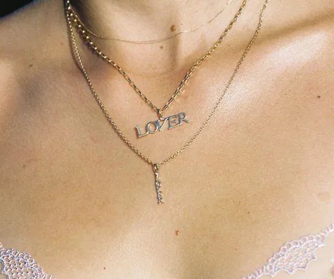 Three gold necklaces layered on a woman's neck, one reads "LOVER," in a close-up shot.