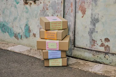 Stack of gift boxes with colorful labels leaning against a textured wall.