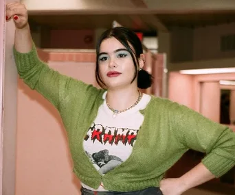 Actress leaning against a wall in a green cardigan and graphic tee with a confident expression.