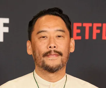 A man with a beard stands in front of a backdrop featuring a partial Netflix logo.