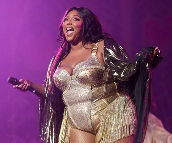 Singer performing on stage in a gold outfit, holding a microphone, with vibrant stage lighting.