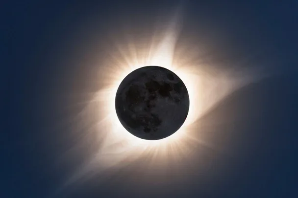 A solar eclipse with the moon covering the sun, revealing the sun's glowing corona in the sky.