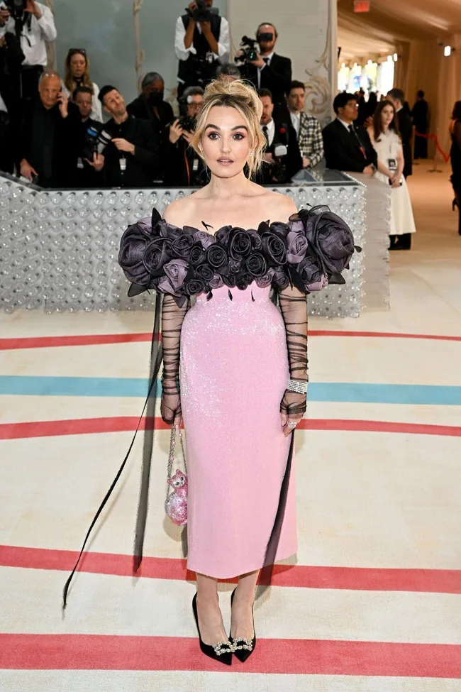 Woman in a pink dress with black rose details at the Met Gala 2023, posing on the red carpet.