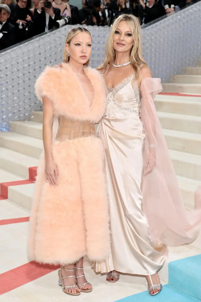 Two women in elegant pastel gowns pose together on a staircase at the Met Gala, surrounded by photographers.