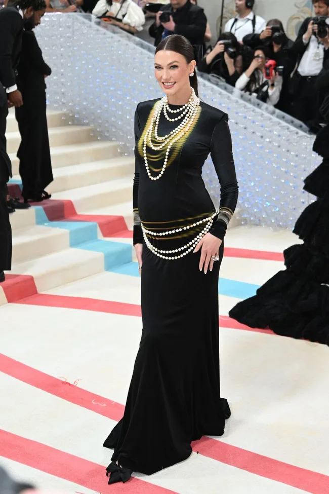 Model in a sleek black gown with pearl necklaces at the Met Gala 2023, smiling on the red carpet.