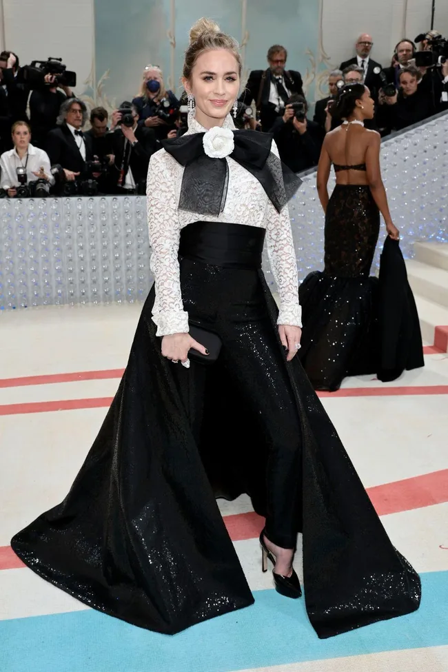 A woman in a black dress with lace sleeves and a large bow poses on the Met Gala 2023 red carpet.