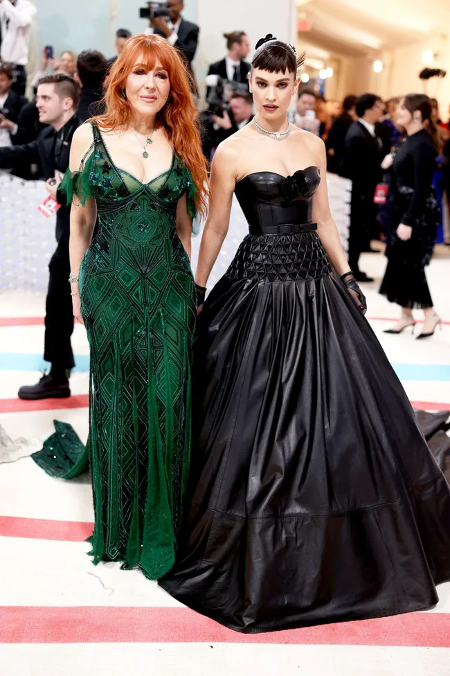 Two women in elegant gowns at a formal event; one in green, the other in black leather.