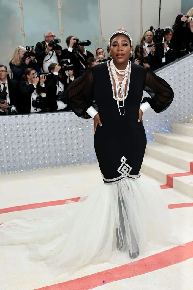 Serena Williams at the Met Gala 2023 in a black dress with sheer sleeves, pearl necklace, and tulle train.