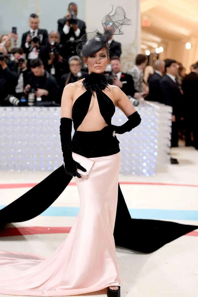 A woman in a pink and black gown with a dramatic hat poses for cameras at the 2023 Met Gala.