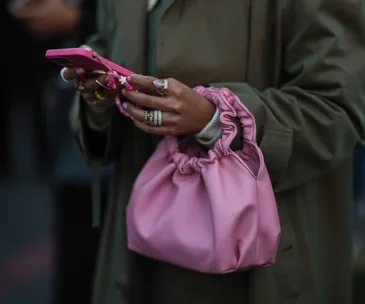 A person wearing rings and holding a pink drawstring bag and a pink phone with charms.