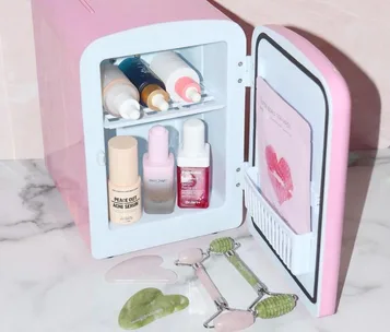 Mini pink fridge with skincare products and jade rollers on marble countertop.