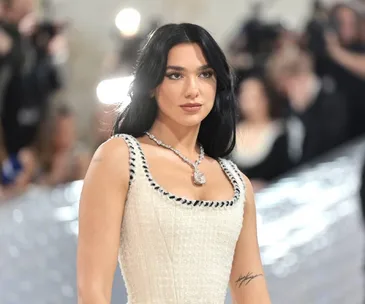 Dua Lipa at the Met Gala in an elegant white dress with a low neckline and statement necklace.