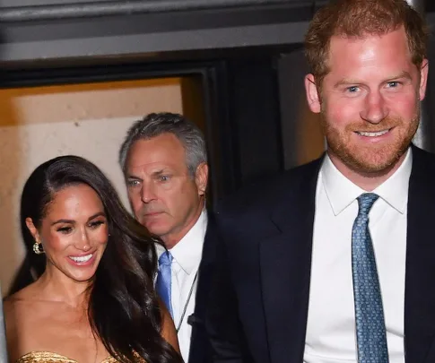 Prince Harry and Meghan Markle smiling, departing an event with a security guard.