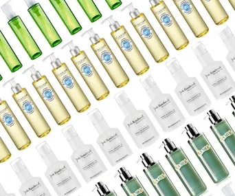 Various bottles of cleansing oils arranged in a diagonal pattern, featuring brands like L'Occitane, Josie Maran, and La Mer.