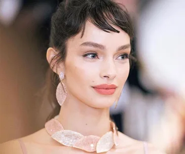 Woman with smooth skin, wearing elegant makeup and accessories, looking sideways in a soft-focus setting.