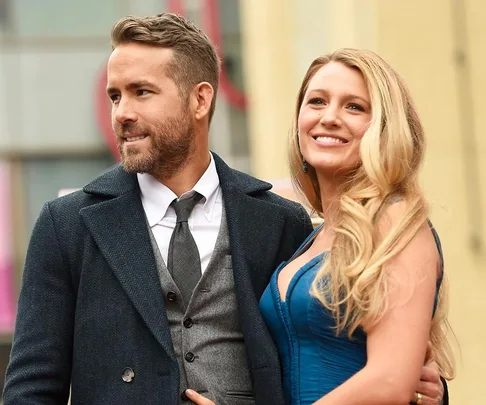 A couple poses together, the man in a dark suit and the woman in a blue dress, both smiling warmly.