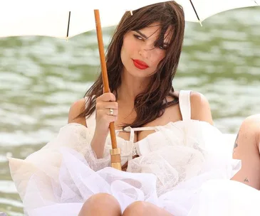 A model in a white dress and red lipstick holds an umbrella by a lake at Jacquemus Fall 2023 show in Versailles.