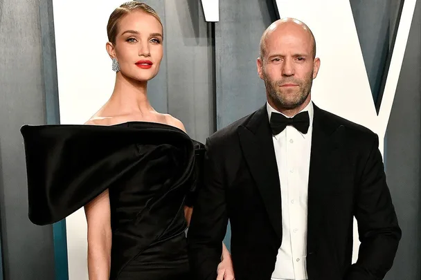 A couple, dressed in formal black attire, pose together at a glamorous event.