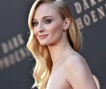 Blonde woman in a strapless dress at "Dark Phoenix" event, smiling with long hair styled to one side.