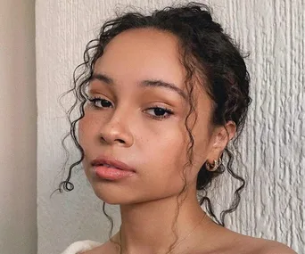 Woman with frizzy hair styled in loose curls, wearing hoop earrings, showcasing a natural makeup look.