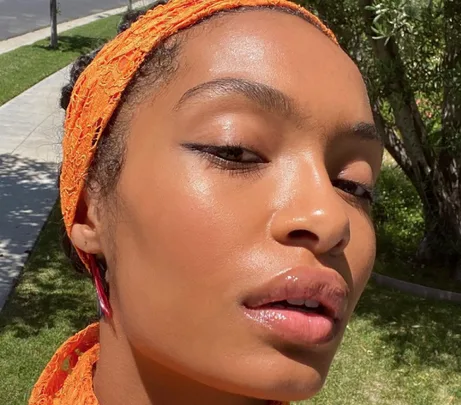 A person outdoors, wearing an orange headscarf with glowing skin.