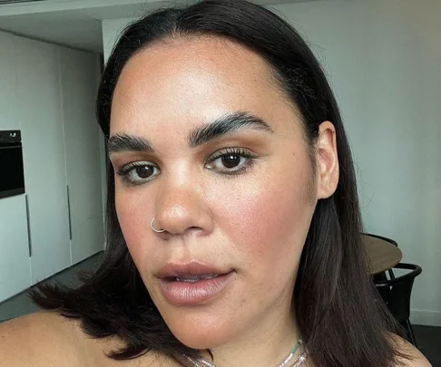 Woman with dark hair and a nose ring taking a selfie in a modern kitchen setting.