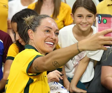 Soccer player in yellow jersey takes a selfie with a smiling young fan, crowded background.