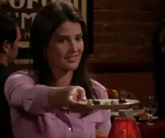 A woman with long brown hair offers a plate of olives in a dimly-lit restaurant.