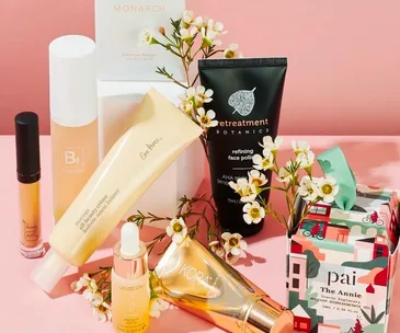 A collection of beauty products, including creams and oils, surrounded by small white flowers on a pink background.